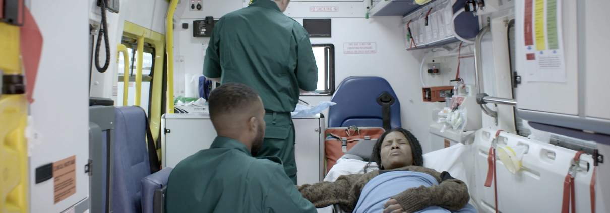 In the back of an ambulance, two paramedics tend to a patient who has recently experienced a miscarriage